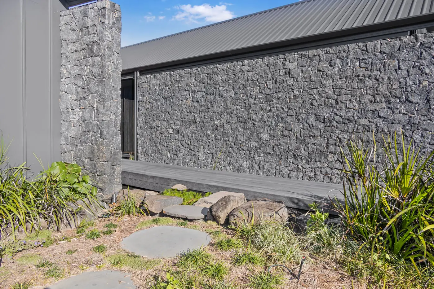 Dry-stacked stone wall, timber bench and stepping stones through planting at the Yandina project