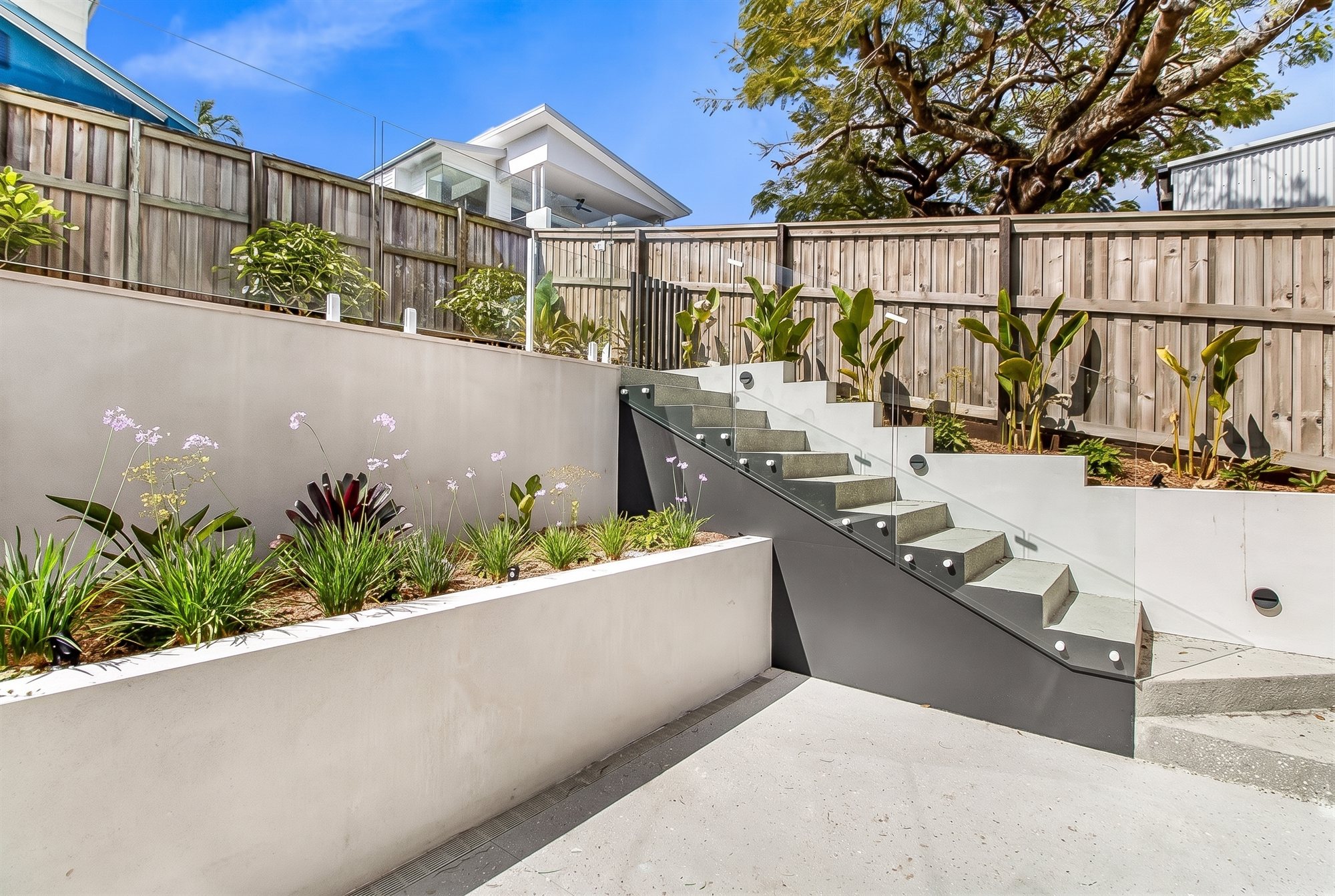 Rendered concrete retaining walls terraced into planters, with concrete steps and a drainage channel