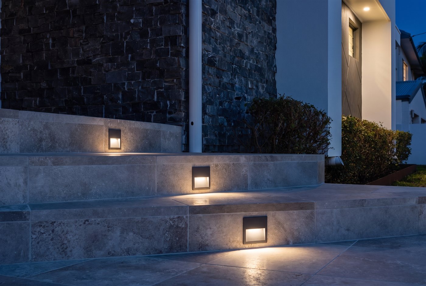 Recessed step lights lit at night in travertine stairs beside a stone wall